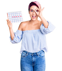 Sticker - Young beautiful woman with pink hair holding heart calendar smiling happy doing ok sign with hand on eye looking through fingers