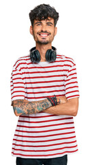 Poster - Young hispanic man listening to music using headphones happy face smiling with crossed arms looking at the camera. positive person.