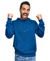 Wall Mural - Young hispanic man wearing casual clothes screaming proud, celebrating victory and success very excited with raised arms