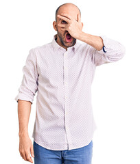 Wall Mural - Young handsome man wearing elegant shirt peeking in shock covering face and eyes with hand, looking through fingers with embarrassed expression.