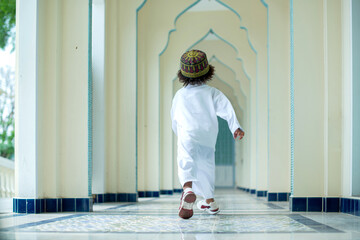 Back view, Muslim child boy in traditional clothes running in the mosque hallway