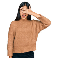 Poster - Beautiful young asian woman wearing casual winter sweater peeking in shock covering face and eyes with hand, looking through fingers with embarrassed expression.