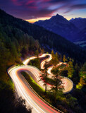 Fototapeta Uliczki - The mountain pass of Maloja, Switzerland. A road with many curves among the forest. A blur of car lights. Landscape in evening time. Large resolution photo for travel
