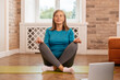 © puhhha - Relaxed woman doing yoga in casual clothing in home living room. Senior woman relaxing in yoga with.eyes closed