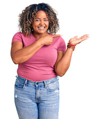 Wall Mural - Young african american plus size woman wearing casual clothes amazed and smiling to the camera while presenting with hand and pointing with finger.