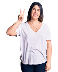 Wall Mural - Young beautiful brunette woman wearing casual t-shirt showing and pointing up with fingers number two while smiling confident and happy.