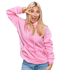 Wall Mural - Young blonde woman wearing casual sweatshirt doing peace symbol with fingers over face, smiling cheerful showing victory