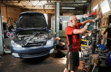 Professional mechanic, repairman, worker holding screwdriver, fixing car. Hardworking man standing in workshop, garage, working with equipment. Concept of manual work.