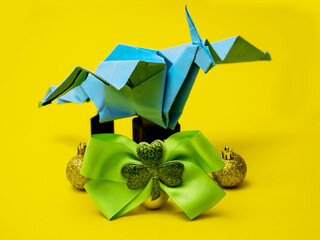 Blue paper origami dragon on golden balls and green ribbon with Irish shamrock on yellow background. Year of powerful creature in Ireland. Hand made craft. Chinese horoscope.