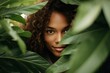 Portrait of young and beautiful latin woman with perfect smooth skin is hiding behind giant tropical leaves. Banner for beauty skin body care, spa salon, bio eco cosmetics concept.