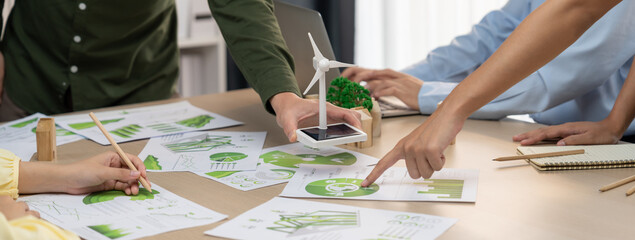 Wall Mural - Windmill model represented renewable energy and wooden block represented eco city was placed on green business meeting table with environmental document scatter around. Front view. Delineation.