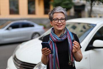 Poster - A mature woman, holding a smartphone, sits confidently in a car, ready for a journey, embodying a business-savvy and elegant vibe.