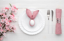 Easter Holiday Table Setting With Egg On Plate And Cutlery, Sakura Blossom, Pink Spring Flowers. White Wooden Background. Top View, Flat Lay. Lunch Or Dinner Invitation Design. Food Concept.