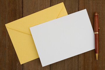 Wall Mural - Blank greeting card with yellow envelope and pen on wood