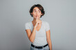© My Ocean studio - Photo of young cute woman posing saying hush be quiet with finger on lips shhh gesture isolated on gray background, studio shot. Lifestyle and people emotions concept.