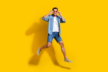 Poster - Full body photo of funky optimistic man dressed denim shirt shorts jumping touching glasses isolated on vivid yellow color background.
