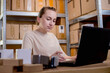 © volody10 - Female warehouse worker online store owner using laptop at work preparing parcel boxes checking ecommerce shipping online retail e commerce store order fulfillment in dropship delivery post office.