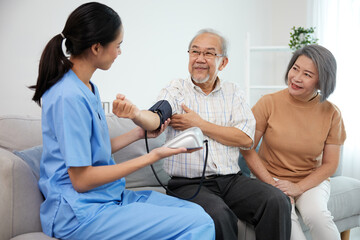 Wall Mural - caregiver or nurse measure blood pressure to senior man on sofa