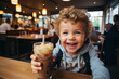 Happy smiling cheerful toddler kid smiling laughing while she holds in hands smoothie drink milkshake with cream beverage with straw. Little child spend time leisure in indoor restaurant bar