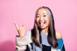 Photo of overjoyed indonesian girl tongue out demonstrate heavy metal symbol isolated on pink color background