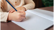 © Angela - Close em mão de uma criança que está escrevendo em um caderno. Conceito de volta às aulas.