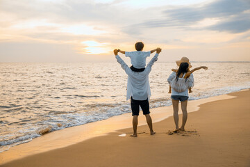 Wall Mural - Father carrying son and Mother carrying daughter on shoulder walking summer beach, Parents carrying children on shoulders at beach on sunset, Family on holiday summer vacation, Happy family in holiday