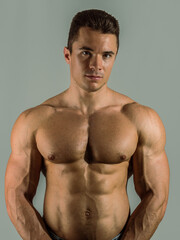 Shirtless young male bodybuilder in studio portrait, looking at camera on neutral background, showing muscular torso and body