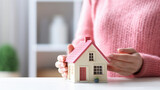 Fototapeta  - Woman's hands gently holding a miniature house model, symbolizing home ownership or real estate