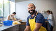 © MP Studio - Smiling man in a cleaning service uniform with colleagues in the background, indicating a professional cleaning team at work.