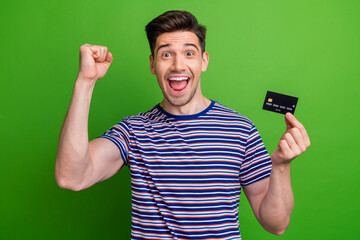 Sticker - Photo of overjoyed cheerful person raise fist arm hold demonstrate debit card isolated on green color background