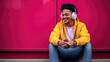 © MP Studio - Joyful young man with white headphones, with a vibrant pink wall in the background, enjoying music.
