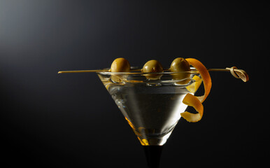 Classic dry martini cocktail with green olives and lemon peel on a black background.