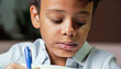 Um menino negro, concentrado, lendo e escrevendo em um caderno. Conceito de retorno às aulas.