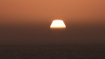 Wall Mural - Sunrise time lapse over large body of water with sun rising through thick haze becoming a bright and hot day.