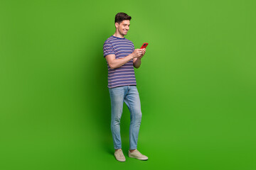 Canvas Print - Full size photo of intelligent optimistic guy dressed striped t-shirt jeans read sms on smartphone isolated on green color background