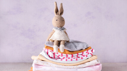Wall Mural - Stack of different baby clothes and knitted bunny toy on light background