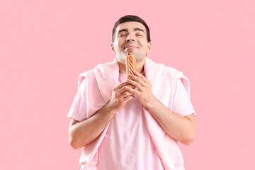 Wall Mural - Happy young man with tasty french hot dog on pink background