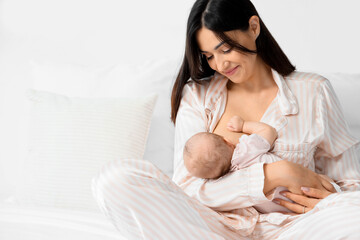 happy mother breastfeeding her little cute baby in bedroom