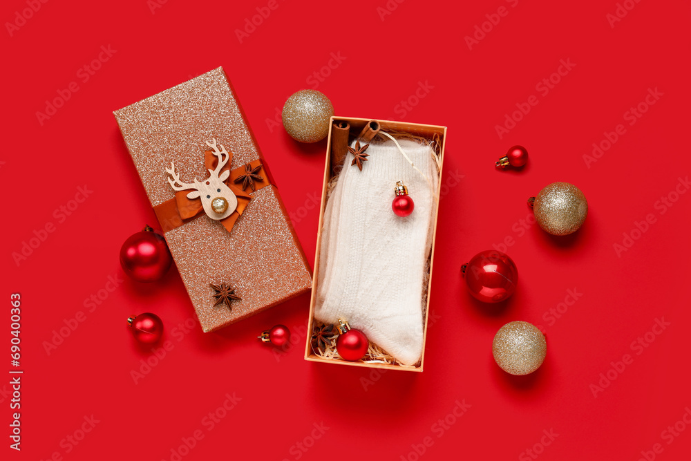 Gift box with knitted socks and Christmas balls on red background