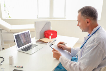 Wall Mural - Mature doctor video chatting with patient on laptop in office