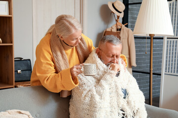 Wall Mural - Mature woman giving her sick husband cup of tea at home