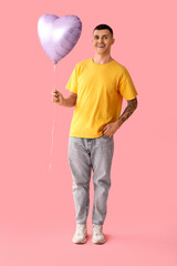 Poster - Happy young man with heart shaped air balloon on pink background