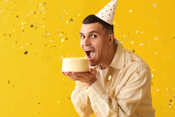 Poster - Young man in party hat with sweet cake and confetti celebrating Birthday on yellow background