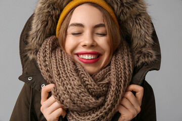 Wall Mural - Beautiful young happy woman in warm winter clothes on grey background