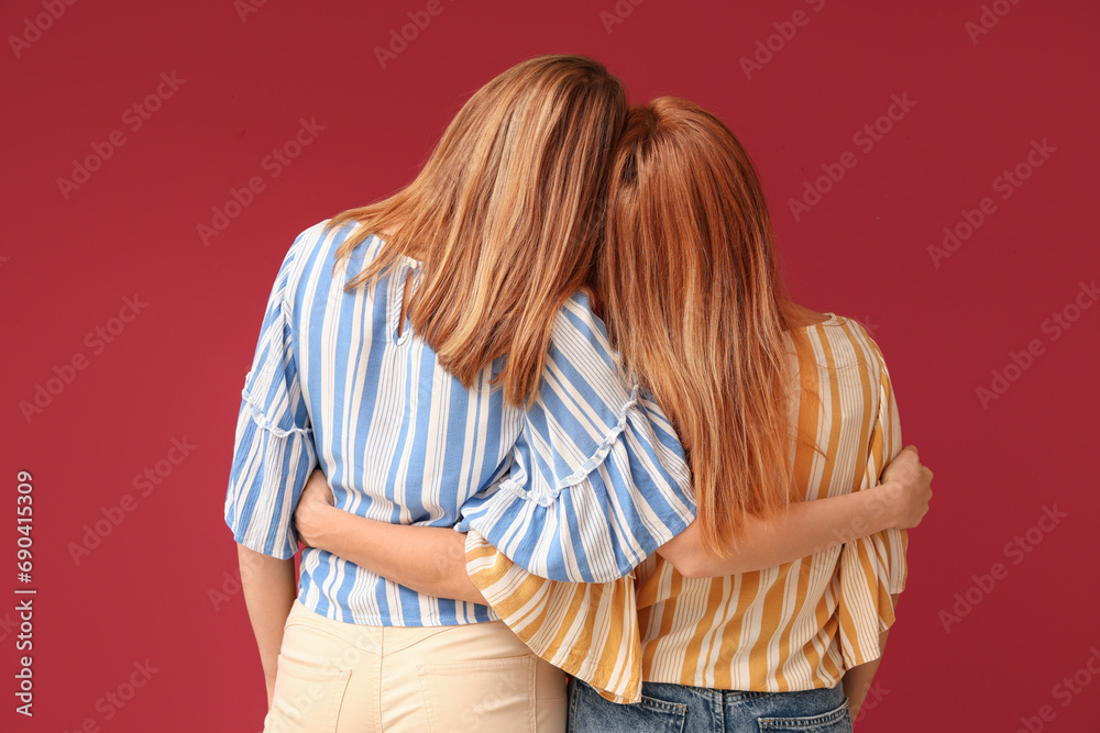 Mature woman hugging her young daughter on red background. International Hug Day