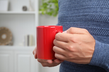 Poster - Man holding red mug at home, closeup. Mockup for design