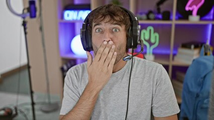 Poster - Shocked young man, covering his mouth in surprise, caught off guard gaming. expression of silent fear in a dark gaming room