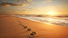  The Footprints Of Two People Are In The Sand On The Beach As The Sun Sets Over The Ocean Behind Them.