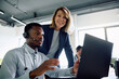 © Drazen - Black businessman with headset working on laptop while female CEO is supervising him in office.