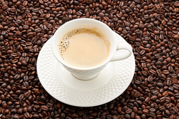 Wall Mural - Top view of coffee in white cup place on surface many roasted coffee beans background.